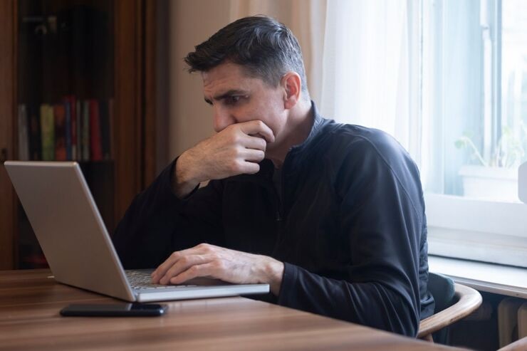 Uomo al PC con mano sulla bocca, legge preoccupato
